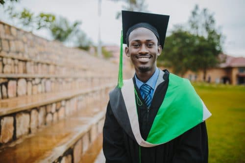 photo of a smiling young sponsored student wearing graduation cap and gown with a green tassle