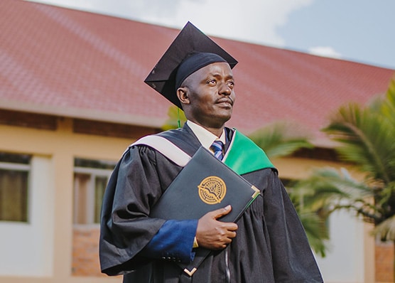 Photo of an Africa College of Theology graduate wearing a cap and robe and holding a diploma